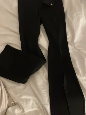 Svarta bootcut kostymbyxor - Säljer ett par svarta kostymbyxor med bootcut passform. Byxorna har en klassisk look med vida ben och midja med hällor för bälte. Perfekta till en snygg outfit när du vill känna dig extra stilsäker.