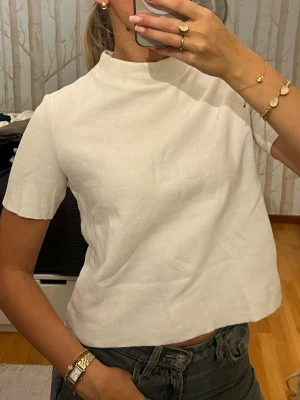 Vit topp från Zara - Vit, stilren topp från Zara med hög hals och korta ärmar. Modellen är rak och något croppad, vilket ger en modern vibe. ”Stickad” och mjuk. Perfekt att matcha med jeans eller kjol för en clean look. Passar xs-m!🫶🏼