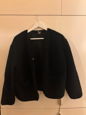 Svart teddyjacka från H&M  - En mysig svart teddyjacka från H&M Divided i storlek S. Jackan har en rund hals, knappar framtill och två fickor💘💘