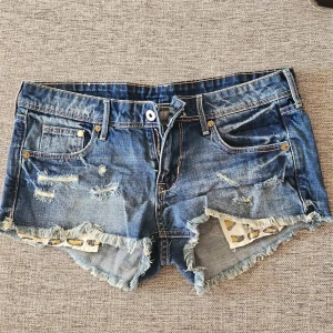 Blå jeansshorts - Snygga blå jeansshorts med slitna detaljer och fransar. Shortsen har en låg midja och leopardmönstrade fickor som ger en cool touch. Perfekta för en avslappnad stil.