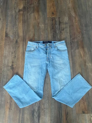 Jacob Cohen ljusblå jeans Style 688 - Jacob Cohen jeans i ljusblå tvätt, modell Style 688. Klassisk femficksdesign med orange kontrastsömmar och broderad J på myntfickan. Rak passform och knappgylf med märkets logga. Tillverkade i mjukt bomullsjeansmaterial för en skön känsla.