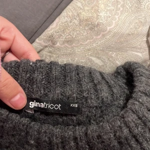 Mörkgrå stickad tröja Gina Tricot - Mysig mörkgrå stickad tröja från Gina Tricot i storlek XXS. Tröjan har breda, långa ärmar och ribbad struktur med slits på sidorna. Perfekt för dig som gillar oversized känsla och vill ha något riktigt comfy till höst och vinter.