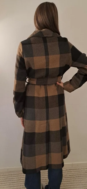 Rutig kappa med bälte från Indiska - Snygg lång rutig kappa från Indiska i bruna och svarta toner. Modellen har omlottstängning med bälte i midjan. Storlek xs men jag tycker den sitter mer som en S, jag är 167 cm och den sitter lite stort även om jag har kofta under. Köpt för 1500kr tror jag och har inte använt den ofta. 🤎🤎Pris går absolut att diskutera.