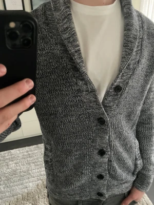 Grå stickad kofta från HM - Säljer en grå stickad kofta från HM i storlek S, modellen är ca 180cm. Hör av dig vid funderingar!