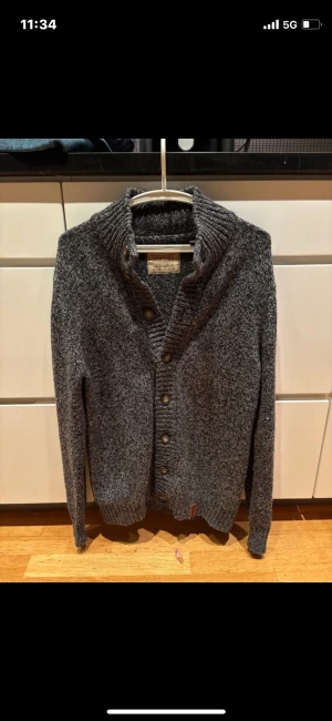 Grå stickad cardigan - Säljer en gråmelerad stickad kofta från Esprit med ribbad krage och knappar framtill. Koftan har långärmad passform och är tillverkad i mjukt material som håller dig varm. Perfekt för dig som gillar chill och stilren look.