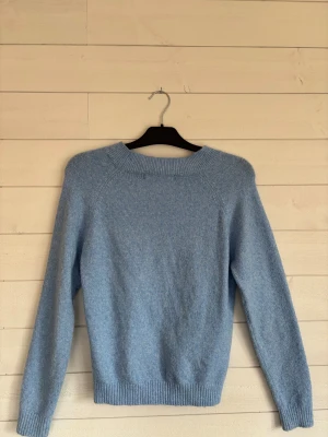 Ljusblå stickad tröja med rund hals - Mysig ljusblå stickad tröja med rundad hals och ribbade muddar vid ärmslut och nederkant. Tröjan har en enkel, klassisk design och är långärmad, perfekt för att hålla värmen under kyliga dagar. Passar dig som gillar stilrena och softa plagg.