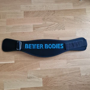 Svart träningsbälte Better Bodies XS - Säljer ett svart träningsbälte från Better Bodies i storlek XS. Bältet har en bred, ergonomisk form och är tillverkat av neopren och polyester. Det har ett stort blått Better Bodies-tryck och justerbart kardborreband för smidig passform.
