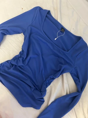 Blå långärmad topp från SHEIN XS - Säljer en blå långärmad topp från SHEIN i storlek XS. Toppen har en fyrkantig urringning och snygga rynkade detaljer på sidorna som ger en cool form. Materialet är mjukt och stretchigt, perfekt för dig som gillar en slim passform.