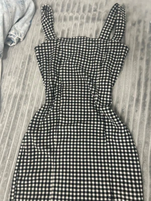 Svartvit rutig klänning H&M S - Supersnygg svartvit rutig klänning från H&M i storlek S. Modellen är kort med breda axelband och en liten slits framtill för extra edge. Passformen är slim och tyget är mjukt och stretchigt, perfekt för dig som gillar trendiga och bekväma outfits.