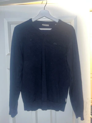 Mörkblå stickad tröja Lindbergh S - Snygg mörkblå stickad tröja från Lindbergh White i storlek S. Tröjan har v-ringad hals och långa ärmar, med diskret logga på bröstet. Perfekt för dig som gillar stilrena och klassiska plagg med skön passform.