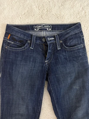 Robin's lågmidjad bootcut jeans🤍 - Sjukt snygga  mörkblå jeans i storlek W24 från märket ”Robin's Jeans”.🖤🖤 broderade svarta vingar på bakfickorna och nitar på myntfickan. Inga defekter och helt oanvända, säljer då de är för små för mig!! Skriv gärna om ni har några frågor 🥰