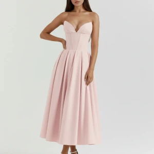 Ljusrosa axelbandslös långklänning - Supersnygg ljusrosa långklänning med axelbandslös design och djup v-ringning. Klänningen har en figurnära korsettliknande överdel och ett utsvängt, veckat midilångt kjolparti. Perfekt för dig som vill ha en elegant och feminin look. Materialet känns slätt och har fin struktur.storlek Xs