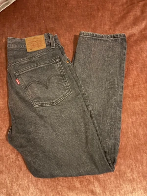 Levi's 501 grå jeans W27 L26 - Svarta Levi's 501 jeans med klassisk femficksdesign och raka ben. Jeansen har  knappgylf och den ikoniska läderpatchen bak. Materialet är slitstarkt denim i bomull och passformen är straight. Inga defekter.