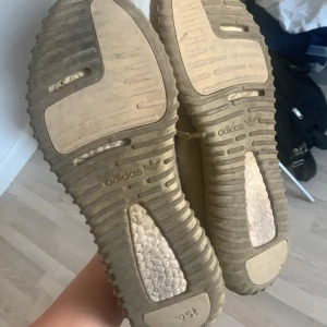 Beige adidas Yeezy Boost 350 sneakers - Säljer ett par beige adidas Yeezy Boost 350 sneakers med stickad ovandel och klassisk ribbad sula. Skorna har snörning och en rund tå, perfekt för dig som gillar streetwear och vill ha något unikt på fötterna. Självklart äkta som man ser på bilderna. Ända negativa är ett den har släppt lite vid stortån på höger skon enkelt fix därav priset 