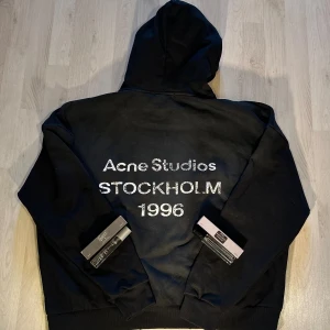 Acne Studios Hoodie - Svart hoodie från Acne Studios. Köpt på Tradera. Säljer då den inte passade mig. Storlek M men skulle säga att den kan passa L också då den är oversized. Inga skador eller liknande. Två parfym flaskor följer med också! 