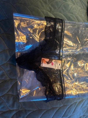 Svarta spetsdetaljerade trosor, stlS - Snygga svarta trosor med transparent mesh och spetsdetaljer. Trosorna har tunna band och dekorativa rosetter framtill för en extra touch. Perfekt för dig som gillar en stilren och sexig look.