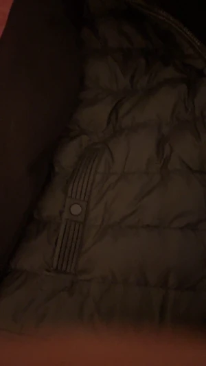 Svart pufferjacka med huva - Svart pufferjacka med huva och hel dragkedja framtill. Jackan har quiltad kropp, släta svarta ärmar och två fickor med snygga ribbade detaljer och knappstängning. Perfekt för kalla dagar och har en clean, modern look.