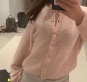 Ljusrosa kofta med knappar gina - Säljer en supermjuk ljusrosa kofta med knappar hela vägen framtill. Koftan har långärmad design och är gjord i ett fluffigt stickat material som känns riktigt cozy. Perfekt att slänga på sig när man vill ha en chill och söt look.