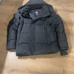 Canada goose Wyndham grå - Säljer en svart dunjacka från Canada Goose i storlek L som även passar M i läng och bredd och S i längdenoch lute baggy i bredden men funkar.Jackan har huva, flera fickor med dragkedja och tryckknappar samt den klassiska Canada Goose-loggan på ärmen. Perfekt för kalla vinterdagar och riktigt snygg streetstil.