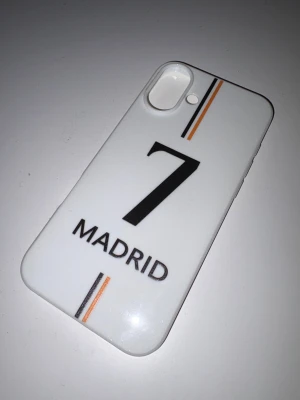 Madrid 7 iPhone 16 plus case - Snyggt skal till iPhone med Madrid-tema och nummer 7. Passar modeller med dubbla kameror och mindre sensor, iphone 16 plus. Skalet är vitt med svarta och orange detaljer, i gott skick utan synligt slitage.