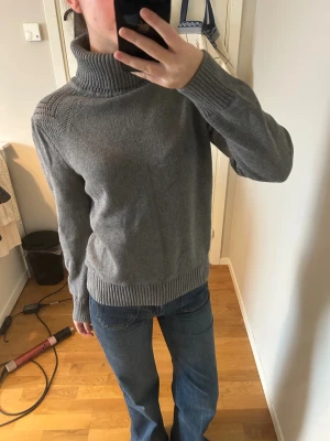 Grå polotröja - Snygg grå polotröja från Jeanswest i storlek xl men är som en M/S. Tröjan har ribbad polokrage, långärmad design och stickat material med fina detaljer vid axlarna. 100% bomull