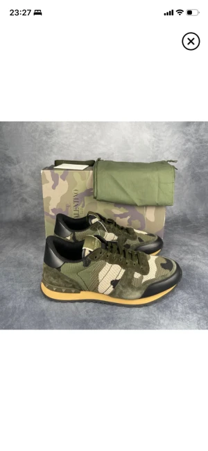 Valentino Rockrunner sneakers camouflage - Snygga Valentino Garavani Rockrunner sneakers med grön, beige och svart camouflage-mönster. Ovandel i mesh och mocka, detaljer i skinn och gummisula med mönstrad undersida. Klassisk snörning och rund tå. Kommer med originalkartong och dustbag.