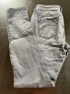 Grå jeans med rak passform - Snygga grå jeans med klassisk femficksdesign och rak passform. Jeansen har bälteshällor och knappstängning framtill. Materialet är mjukt och bekvämt denim, lite stretch, som passar perfekt till en avslappnad stil. Färgen är neutral och lätt att matcha med olika outfits.   Strl M, mått midja tvärs över 35 cm innerben 81 cm