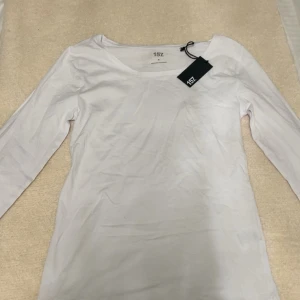 Vit långärmad topp från 157 - En basic vit långärmad topp från 157 med rund halsringning. Tillverkad i mjuk bomull, perfekt att styla med jeans eller kjol. Enkel och stilren design som funkar till många olika looks.
