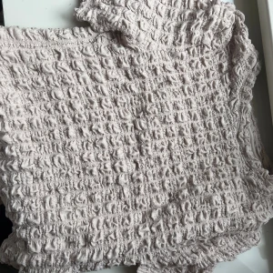 Beige smockad topp från Lindex - Supersöt beige topp från Lindex i smockat tyg med korta ärmar. Toppen har en stretchig och strukturerad yta som ger en cool och trendig look. Perfekt att styla med jeans eller kjol för en chill vibe.