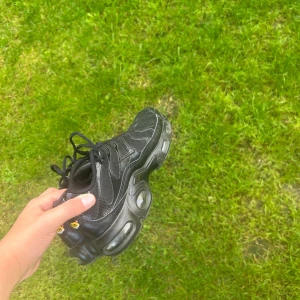 Nike svarta sneakers Air Max TN - Svarta Nike Air Max TN sneakers med coola detaljer och synliga luftbubblor i sulan. Skorna har snörning, mesh och syntetmaterial samt diskret Swoosh-logga på sidan. Perfekta för dig som gillar sportig och street-inspirerad stil.