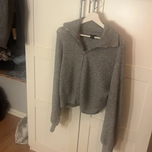 Grå stickad kofta med dragkedja Lindex - Mysig grå stickad kofta från Lindex i storlek M. Koftan har en bred krage, långärmad passform och dragkedja framtill. Ribbad struktur ger en cool vibe och den är perfekt för kyliga dagar.