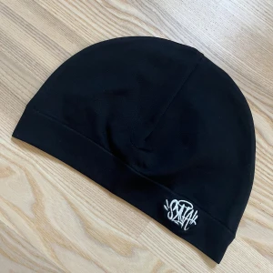 Svart mössa med vit brodyr syna - Svart mössa från Syna med vit broderad logga framtill. Enkel och clean design i mjukt bomullsmaterial, perfekt för att hålla stilen när det är kyligt ute. Sitter tight på huvudet och funkar till de flesta outfits. Oanvänd!!!