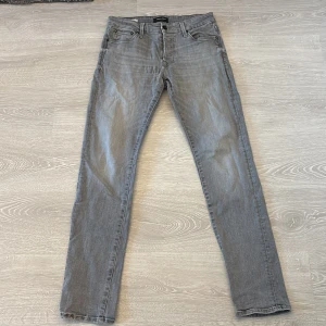Grå slim jeans från Jack & Jones - Slim Glenn jeans från Jack & Jones i en snygg grå tvätt. Klassisk femficksmodell med dragkedjegylf och bälteshällor. Jeansen har en smal passform och raka ben, perfekta för en clean och modern look.