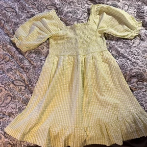 Lime grön och vitrutigt kortklänning - Superfin kort klänning i ljusgul och vit rutig bomull med smock upptill, puffärmar och volangkant nertill. Sitter bekvämt och är ganska luftig.Aldrig använd, säljer då det inte är min stil!