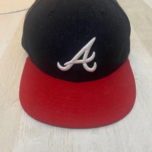 Atlanta Braves keps från New Era 59FIFTY - Säljer en klassisk Atlanta Braves keps från New Era 59FIFTY-serien. Kepsen har svart krona, röd skärm och ett broderat vitt A framtill. MLB-logga baktill. Tillverkad i polyester och har en rak skärm för en sportig look.