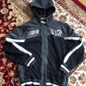 Vintage Camp David hoodie med brodyr och dragkedja - Snygg hoodie från Camp David i svart och mörkgrått med vita detaljer. Tröjan har broderade racing patches och text både fram och bak, hel dragkedja. Passar M/L. Mycket bra skick.