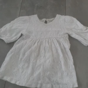 Vit broderad blus från de facto! - Supersöt vit blus från Beebie med broderade detaljer och lätt puffade trekvartsärmar. Blusen har v-ringning och ett luftigt fall, perfekt för en fräsch och romantisk look. Tillverkad i bomull med fina hålbroderier över hela plagget.