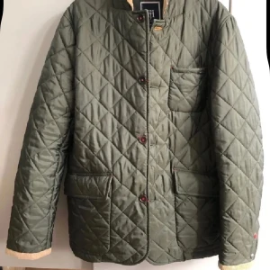 Olivgrön quiltad jacka Hansen & Jacob - Säljer en olivgrön quiltad jacka från Hansen & Jacob. Jackan har beige manchesterkrage, stora fickor framtill och knäppning med knappar. Perfekt för dig som gillar klassisk stil med modern touch. Fodrad och med snygga detaljer på ärmslut och krage. Ny :aldrig använd 