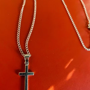 By prisförslag- Silverhalsband med kors 55 cm längd  - Stilrent halsband i silverfärg med en klassisk korsberlock. Kedjan är tunn och har ett enkelt men snyggt uttryck. Perfekt för dig som gillar minimalistiska smycken med symbolisk touch.