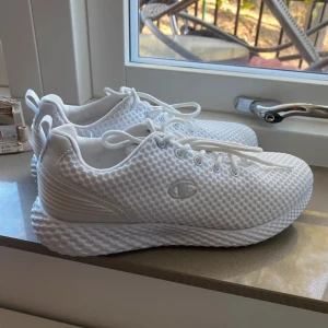 Vita sneakers från Champion - Säljer ett par fräscha vita sneakers från Champion. Skorna har mesh-överdel för extra andningsförmåga, snörning och en chunky sula med mönster. Perfekta för dig som gillar sportig stil och vill ha något lätt på foten.