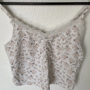 Blommig linnetopp med spets från SHEIN - Supersöt ljus linnetopp från SHEIN med små blommor i beige och svart. Toppen har tunna axelband, spetskant upptill och en lätt rynkning framtill. Materialet är mjukt och stretchigt i bomull och spandex, perfekt för varma dagar.