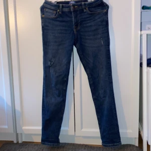 Mörkblå raka jeans från jack and Jones  - Snygga mörkblå jeans från jack and Jones med en femficksdesign och raka ben. Jeansen har diskreta slitningar framtill för en cool look och är tillverkade i robust denim. Perfekta för dig som gillar en tidlös stil med lite edge. Passar dig som 155-165 storlek 152 w26 w28
