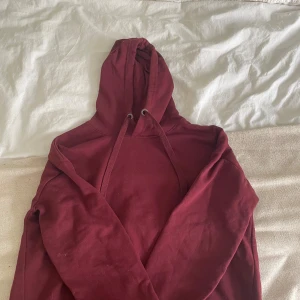 Vinröd hoodie från 157, storlek M - Mysig vinröd hoodie från 157 med huva och snörning. Klassisk modell i mjuk bomullsblandning, perfekt för chill dagar. Snygg och enkel att matcha med jeans eller mjukisbyxor.