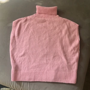 Rosa stickad tröja med polokrage - Mysig rosa stickad tröjamed hög ribbad polokrage och breda ribbade kanter nedtill. Perfekt att slänga över en skjorta eller långärmad tröja för extra värme och stil. Enkel och clean design utan mönster eller detaljer.