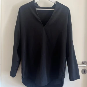 Svart v-ringad blus Gina Tricot - Stilren svart blus från Gina Tricot i storlek 36. Blusen har v-ringning, lång ärm och en något längre bakdel. 