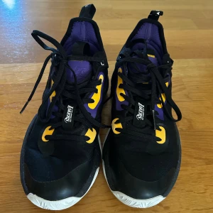 Basket Lakers sneakers svart/lila/gul - Snygga Los Angeles Lakers sneakers i svart med lila och gula detaljer samt Lakers-logga på hälen. Skorna har snörning, vit sula med mönster och cool gradient på sidan. Knappt använda, strl 37