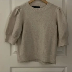 Beige stickad tröja med puffärm - Snygg beige stickad tröja med puffade trekvartsärmar och bred ribbad kant vid hals, ärmslut och nederkant. Perfekt för dig som gillar en enkel men trendig look med lite volym på axlarna.