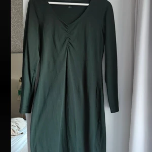 Mörkgrön långärmad klänning Ellos - En stilren mörkgrön klänning från Ellos med lång ärm och v-ringning. Storlek står ej men passar M/L. Använd enstaka gång.