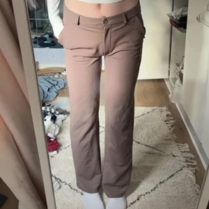 Beige low waist kostymbyxor från Lager 157 - Snygga beige kostymbyxor från Lager 157 i storlek XS. Byxorna har raka ben, normal passform och midja, samt klassiska fickor och hällor för bälte. Perfekta att styla med en crop top eller skjorta för en clean look.