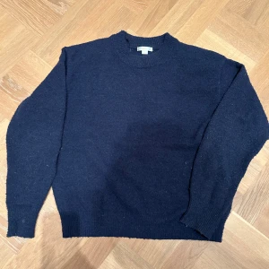 Mörkblå stickad tröja från Gina Tricot - En enkel och klassisk mörkblå stickad tröja från Gina Tricot. Tröjan har rund halsringning, ribbade muddar och är långärmad. Perfekt för lager-på-lager under kyliga dagar.strl 158/164.  Aningens noppig fram och på ärmslut, går absolut att ta bort. 